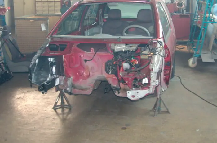 Rote Fahrzeugkarosserie nach einem Unfall, zerlegt und auf Unterstellböcken in der Werkstatt